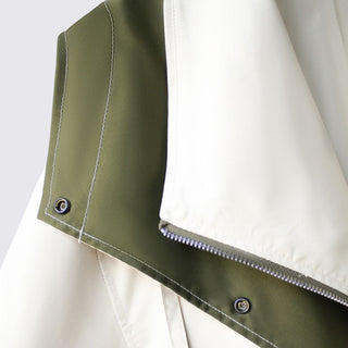 Close-up of a green and white jacket with a zipper and button details on a light gray background.